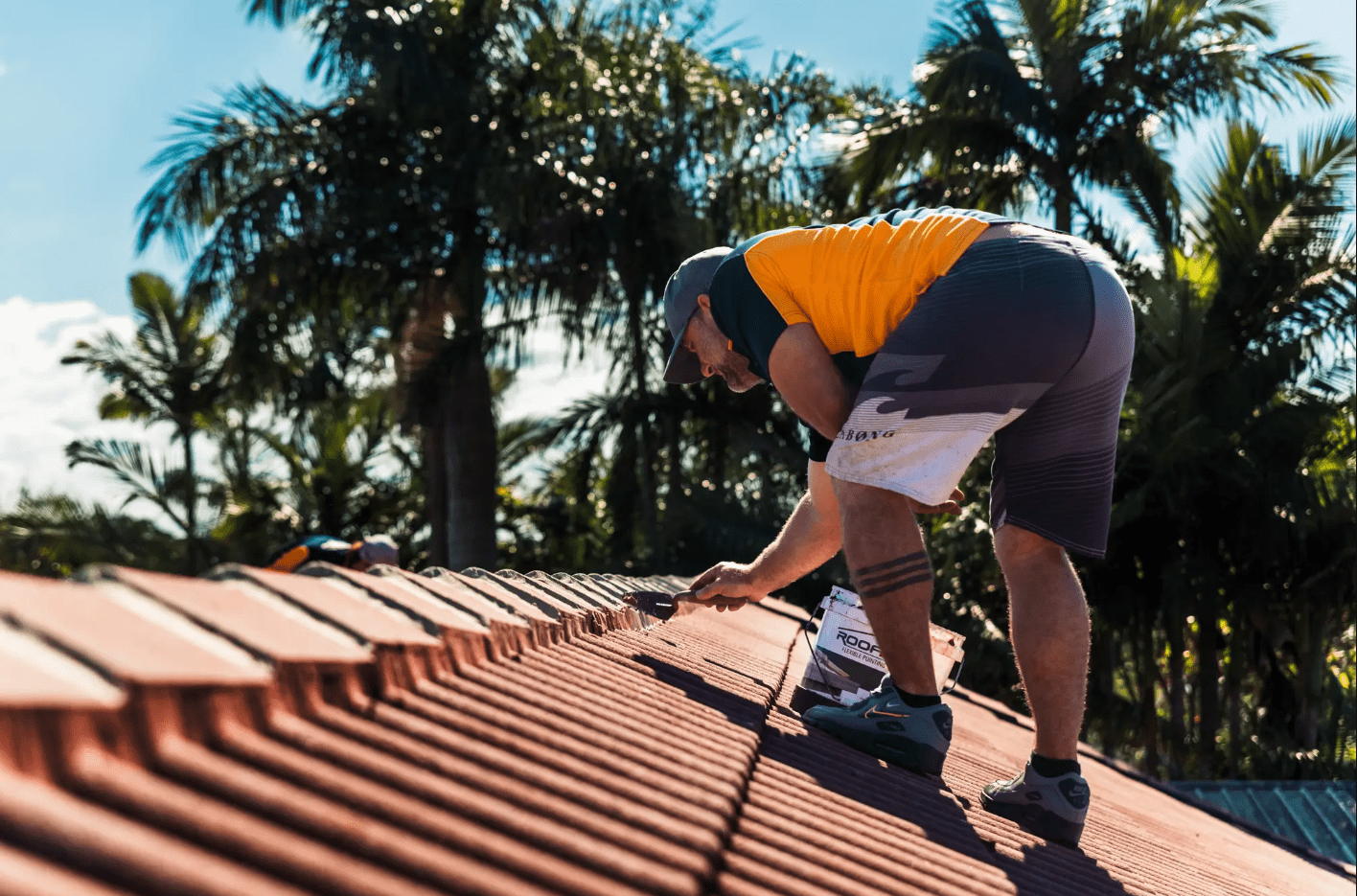 A roofing professional applying flexible pointing compound to the ridge caps of a tile roof in Byron Bay during a sunny day.